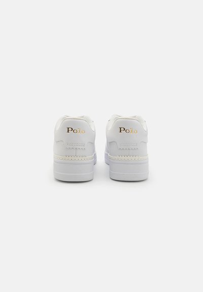 Zapatillas blancas con parte superior de cuero suave, punta redonda, cuello acolchado y acentos texturizados. Presenta un sutil logo dorado de "Polo" en los talones.