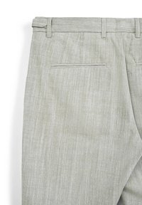 Pantaloni grigi chiari su misura con passanti per cintura e una tasca posteriore a filetto singola, che mostrano la texture del tessuto e i dettagli delle cuciture.