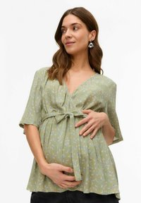 Zelena cvetna oblačila za nosečnice s kratkimi rokavi, V-izrezom, z vezavo spredaj in mehko, strukturirano tkanino. Ima ohlapen kroj, ki ustreza rastočemu trebuhu.