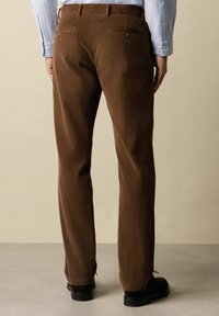 Pantaloni in corduroy marrone con righe verticali, dotati di due tasche posteriori. Il design prevede una vestibilità dritta e una finitura leggermente testurizzata.