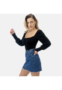 Top nero a maniche lunghe con dettaglio arricciato sul busto abbinato a una mini gonna in denim blu con orlo sfrangiato e tasche frontali.