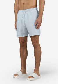 Lyseblå svømmebukser med elastisk liv og snøring. Kombinert med hvite slippers med en bred stroppdesign.