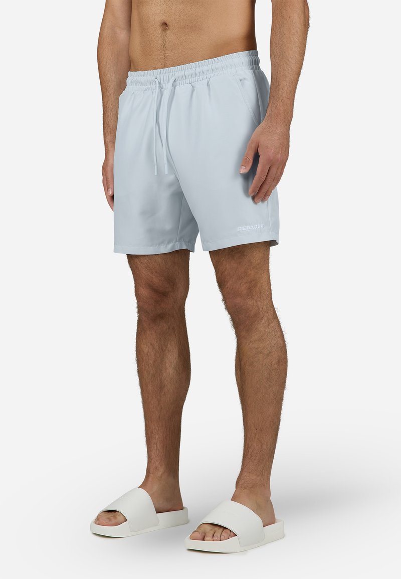 Lyseblå svømmebukser med elastisk liv og snøring. Kombinert med hvite slippers med en bred stroppdesign.