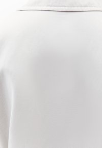 Biała tkanina o teksturowanej powierzchni, z delikatnym połyskiem i klasycznym krojem kołnierzyka. Brak widocznych elementów metalowych lub akcentów.