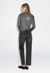 Maglietta grigia a maniche lunghe abbinata a jeans neri in denim a vita alta, dotati di tasche posteriori e una vestibilità rilassata, completata da scarpe nere.