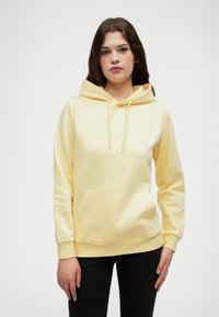 Gul hettegenser med frontlomme, snøring og ribbestrikkede mansjetter. Laget av mykt stoff, har den en subtil logo på brystet.