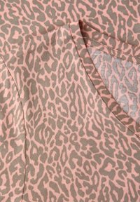 Lähikuva vaaleanpunaisesta ja beigenvärisestä leopardikuvioisesta kankaasta, jossa näkyy sauma ja limittäin olevat reunat, esitellen tekstuurin ja kuviot.
