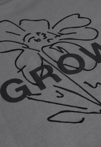 Dessin au trait d’une fleur souriante avec une tige et des pétales, partiellement recouverte par le texte en gras "GROW" sur tissu.
