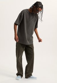 Přehnaně velké šedé bavlněné tričko a volné olivově zelené džíny, doplněné kostkovanými modro-bílými slip-on botami. Minimalistický design.