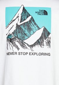 Camiseta blanca con un gráfico de montaña negra sobre un fondo turquesa y el texto "NUNCA DEJES DE EXPLORAR" en negrita negra.