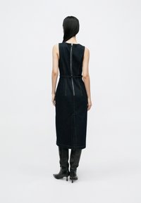 Mörk denimklänning utan ärmar med figurnära silhuett, dragkedja bak och midjebälte. Knälång med minimala sömdetaljer.