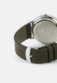 Montre avec bracelet en cuir vert, boîtier en acier inoxydable argenté, surface polie et bracelet texturé. Comprend un cadran rond et une fermeture à boucle.