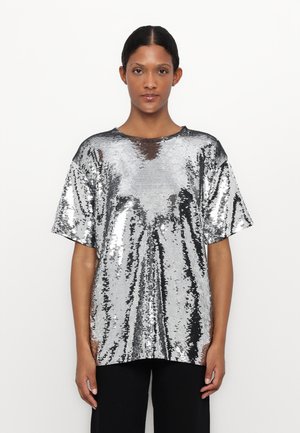 T-shirt oversized in paillettes argentate con maniche corte e scollatura rotonda; texture elegante e lucida con superficie riflettente e leggero drappeggio.