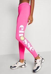 Różowe legginsy z elastycznego materiału z wysokim pasem, z białym napisem i uśmiechniętą buźką po lewej stronie nogawki.