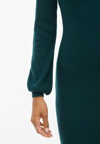 Vestido de punto color teal con mangas largas y acampanadas, y una silueta ajustada. Tejido texturizado con detalles en canalé y puños ceñidos.