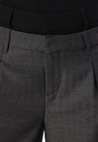 Pantaloni cu model houndstooth în negru și gri, cu o textură netedă; dispune de un tiv solid negru și buzunare laterale.