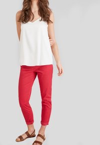 Un haut sans manches blanc avec un décolleté en V, associé à un pantalon rouge fuselé. Sandales avec des brides brunes. Design simple et épuré.