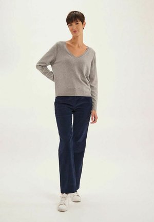 Pull en v gris en tricot, pantalon en velours côtelé bleu marine, baskets blanches. Le pull a des manches longues et un ourlet côtelé ; le pantalon a une coupe droite avec un tissu texturé.