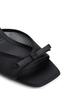 Chaussure noire à bout ouvert dotée d'une tige en tissu texturé, d'un bout carré plat et d'un nœud en satin décoratif à l'avant.