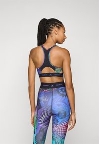 Zwarte sportbeha met kleurrijke accenten en een uitgesneden achterkant, gecombineerd met opnieuw gekleurde leggings met abstracte patronen en texturen.