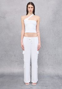 Top corto blanco con una sola tirante, combinado con pantalones blancos holgados que tienen bolsillos tipo cargo y cintura con cordón. Textura suave.