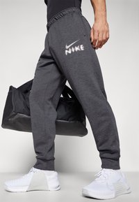Gray athletic sweatpants with an elastic waistband and side pockets, featuring a white Nike logo. Worn with white sneakers and a black gym bag.