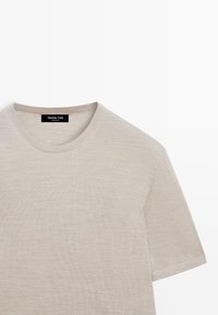 Pull beige à manches courtes en maille fine avec col rond, étiquette Massimo Dutti visible au niveau de l'encolure sur fond blanc.