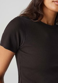 T-shirt nera a maniche corte con scollatura rotonda e design aderente, che presenta una texture liscia e cuciture pulite.
