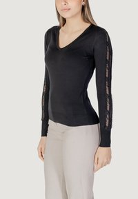 Maglia nera a maniche lunghe con scollo a V, con dettagli in pizzo sulle maniche, realizzata in un tessuto morbido e elasticizzato per un look aderente.