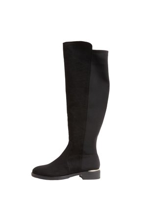 Schwarzer knielanger Stiefel mit flacher Sohle, rundem Zehenbereich und metallischem Detail an der Rückseite der Ferse, seitlich auf weißem Hintergrund gezeigt.