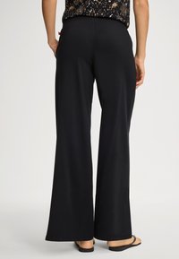 Svarta, vida byxor i mjukt, stretchigt tyg. Har en elastisk midjeband och slät textur; vy bakifrån.