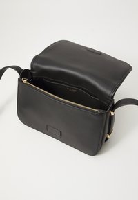 Borsa crossbody in pelle nera con una texture liscia, zip dorata e una tasca frontale. L'interno presenta un logo e ampio spazio.