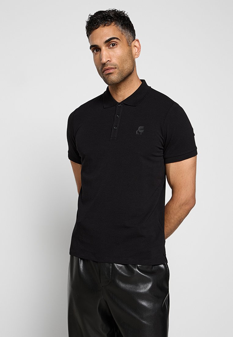 Polo noir en mélange de coton, avec des manches courtes, un col à trois boutons et un logo ton sur ton sur la poitrine gauche. Associé avec un pantalon noir.