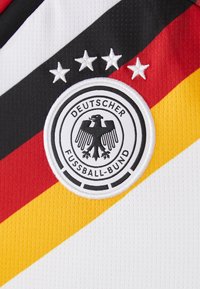 Embleem van het Duitse voetbalteam met zwarte adelaar en vier sterren op een wit shirt met diagonale zwarte, rode en gele strepen.