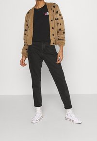 Hnědý pletený cardigan s černými puntíky, černé tričko, černé džíny a bílé vysoké tenisky. Cardigan má velké knoflíky.