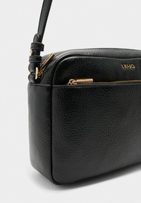 Sac bandoulière en cuir noir avec un fini texturé, accents en métal doré et une poche avec zip. Dispose d'une sangle réglable.