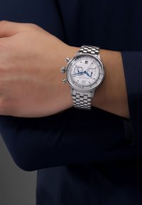 Kronografklocka i rostfritt stål med silverfärgad urtavla, blå detaljer, datumdisplay och en länkarmband, bärs på ett handled.