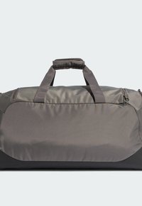 Borsa da viaggio in tessuto grigio con una texture liscia, due manici superiori e una tasca con zip. Presenta una base nera solida e un design minimalista.