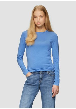Langskes, getailleerd shirt van lichtblauwe katoen. Ronde halslijn, zachte textuur. Gecombineerd met lichtgekleurde spijkerbroek.