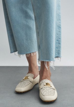 Beige Loafers mit einer strukturierten Oberseite, die ein Monogrammmuster aufweist, goldene Hardware-Akzente und robuste Sohlen, kombiniert mit ausgefranstem blauen Denim.