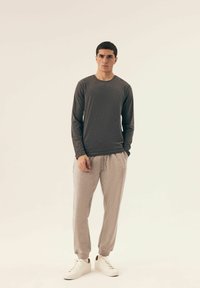 Dunkelgraues Langarmshirt kombiniert mit hellgrauen Jogginghosen. Die Sneakers sind weiß. Die Texturen der Kleidungsstücke wirken weich und haben eine lässige Passform.