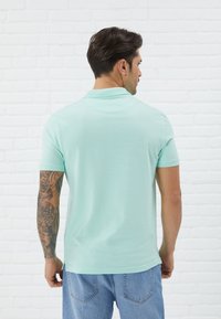 Lyseblå polo med myk tekstur, kort erm og klassisk krage, brukes med denimjeans. Bakside viser et enkelt design.