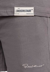 Pantaloncini grigi in cotone con etichetta tessuta "Reichstadt" e dettagli ricamati. Il tessuto ha una consistenza liscia.