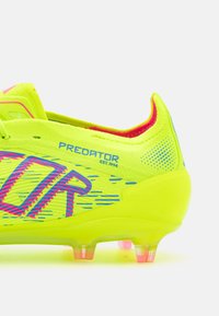 Botín de fútbol amarillo brillante con acentos en azul y rosa. Presenta una parte superior texturizada y una suela moldeada con tapones transparentes rosas.
