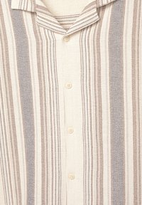 Chemise à boutons avec un fond crème et des rayures verticales marron et gris. Elle présente un col pointu et un tissu léger et texturé.