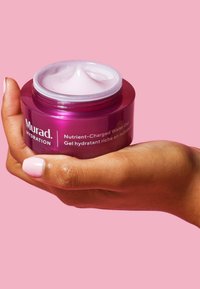 Murad Nutrient-Charged Water Gel i en klar, rund, lila burk som hålls i en hand, med en jämn, ljusrosa gel som syns inuti.