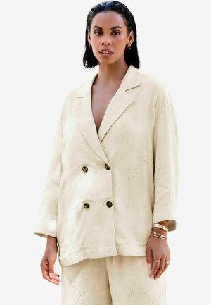 Veste double boutonnage beige clair avec un motif texturé, des revers à cran et deux boutons foncés. Présente des manches amples et une coupe décontractée.