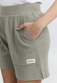 Grå vävda shorts med en texturerad yta, med sidofickor och en etikett märkt "oxmo," designade med resårmidja.