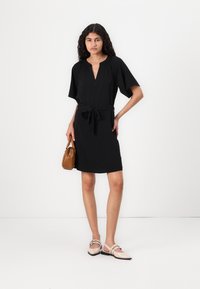 Μαύρο φόρεμα με V λαιμόκοψη και κοντά μανίκια, με σφιξίματα στη μέση και αντίστοιχο κορδόνι. Συμπληρωμένο με μπεζ παπούτσια από πατέντα και καφέ τσάντα.