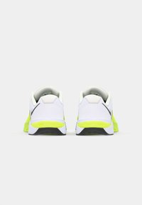 White athletic shoes with neon yellow accents, featuring a sleek design, cushioned heel, and black detailing on the sides.